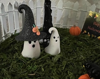 Könnte beinhalten: Eine Miniatur-Halloween-Szene mit einem Hexen-Geist, einem Geist und Kürbissen vor einem weißen Lattenzaun. Die Szene ist in einem Bett aus grünem Moos angelegt.