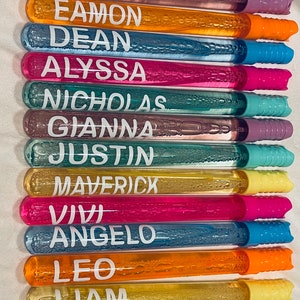 May include: A set of 12 colorful bubble wands with names written on them. The names are Charlotte, Eamon, Dean, Alyssa, Nicholas, Gianna, Justin, Maverick, Vivi, Angelo, Leo, and Liam.