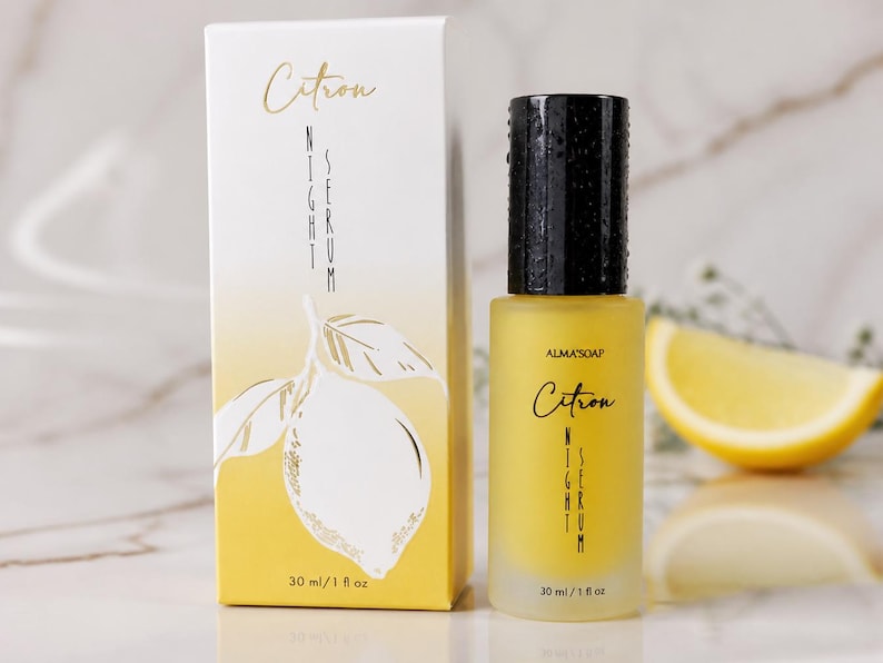 May include: A yellow glass bottle of Citron Night Serum with a black cap, next to a matching box. The box and bottle feature the text "Citron Night Serum" and a lemon illustration. A lemon slice is in the background. The bottle contains 1 fl oz.