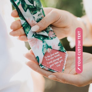 May include: A white bow tie with a pink and green tropical leaf pattern. A pink leather tag is attached to the bow tie with the text "To the first man I've ever loved, I will always be your little girl - Erin".
