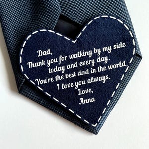 May include: Navy blue tie with a heart-shaped patch. The patch has white stitched edges and white text that reads "Dad, Thank you for walking by my side today and every day. You're the best dad in the world. I love you always. Love, Anna."