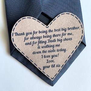May include: A brown heart-shaped tag with a message for a big brother. The tag is attached to a black tie. The message reads: "Thank you for being the best big brother, for always being there for me, and for filling Dad's big shoes & walking me down the aisle today. I love you! Love, your lil sis."
