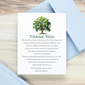 May include: A white card with a green tree illustration and the words "THANK YOU" in green. The card is accompanied by a light blue envelope, suitable for sending a thank you note.