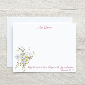 May include: White card with pink floral design and the text "Mia Garcia" at the top. The bottom of the card has the text "May the God of hope fill you with Joy and peace. Romans 15:13"