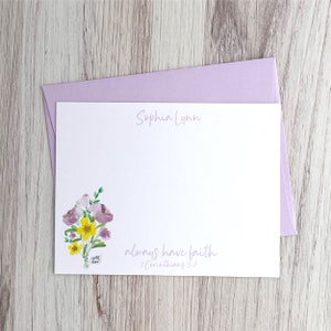 May include: A white card with a purple envelope. The card has a watercolor illustration of a bouquet of pink and yellow flowers. The text "Sophia Lynn" is at the top of the card. The text "always have faith 2 Corinthians 5:7" is at the bottom of the card.