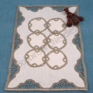 May include: A white linen table runner with a delicate lace border and a pattern of five beige circles in the center. The runner is on a blue surface and there are three wooden bobbins on the right side of the image.