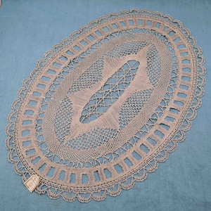 Peut inclure: Un délicat napperon en dentelle de forme ovale avec un motif floral au centre. Le napperon est fait de fil blanc et a un bord festonné.