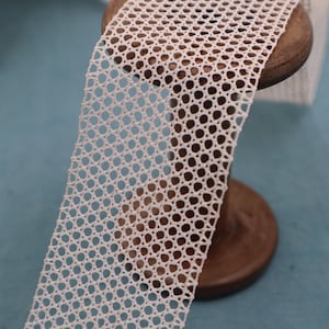 Peut inclure: Garniture en crochet blanc avec un motif circulaire. La garniture est enroulée sur une bobine en bois.