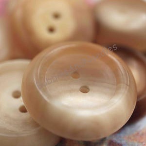 May include: A close-up of four beige buttons with two holes each. The buttons are smooth and have a slight sheen.