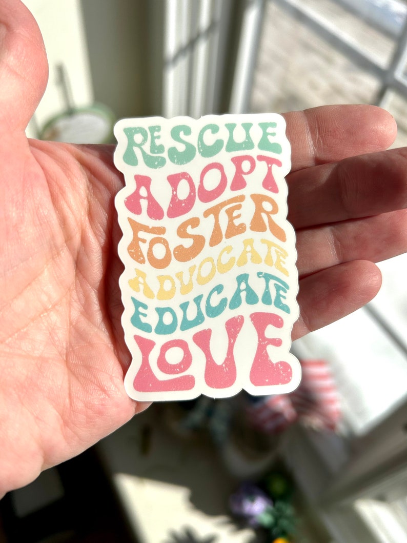 May include: A sticker with the words "Rescue, Adopt, Foster, Advocate, Educate, Love" in a rainbow of colors. The words are in a retro font style.