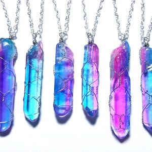May include: Six iridescent crystal necklaces. Each crystal is a different shade of blue, purple, and pink, wrapped in a silver wire cage and suspended from a silver chain. The crystals are elongated and vary slightly in shape.