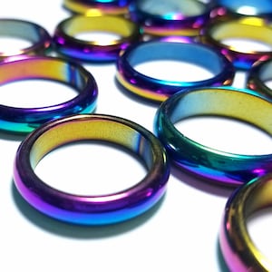 May include: A collection of iridescent rings in various shades of blue, purple, and gold. The rings are made of a shiny, metallic material and are arranged on a white surface. The rings have a smooth, polished finish.