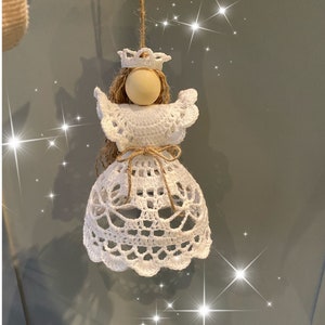 Könnte beinhalten: Weißer Häkelengel-Anhänger mit einem Holzkopf und einer Krone. Der Engel hängt an einer Schnur.