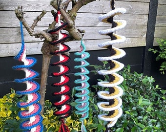 May include: Four colorful crocheted spiral ornaments hanging from a tree branch. The ornaments are made of yarn in red, white, blue, black, yellow, and teal.