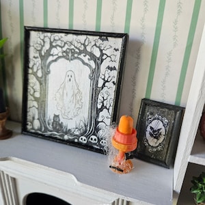 May include: A black framed picture with a spooky Halloween scene of a ghost in a tree with a black cat and skulls. A smaller black framed picture with a black bird and a spider web. A small orange and black candle holder with a spider web.