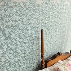 May include: A miniature bedroom scene featuring a patterned wallpaper in shades of green and white. A wooden bed frame with a floral pillow and white bedding is visible, creating a cozy, inviting atmosphere.