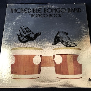 May include: Album cover for "Bongo Rock" by The Incredible Bongo Band. The cover features a silver background with the band's name and album title in black text. Two black hand silhouettes are above a pair of wooden bongos.