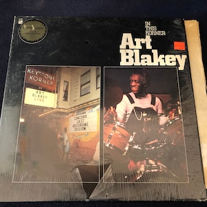 May include: A vintage vinyl record album titled "In This Korner" by Art Blakey. The album cover features a black background with the artist's name in large white letters. The album is sealed in plastic and includes a photo of Art Blakey playing the drums.