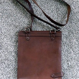 May include: A brown leather crossbody bag with a long adjustable strap. The bag has a rectangular shape with a flap closure and metal hardware. The bag is made of a smooth, dark brown leather.