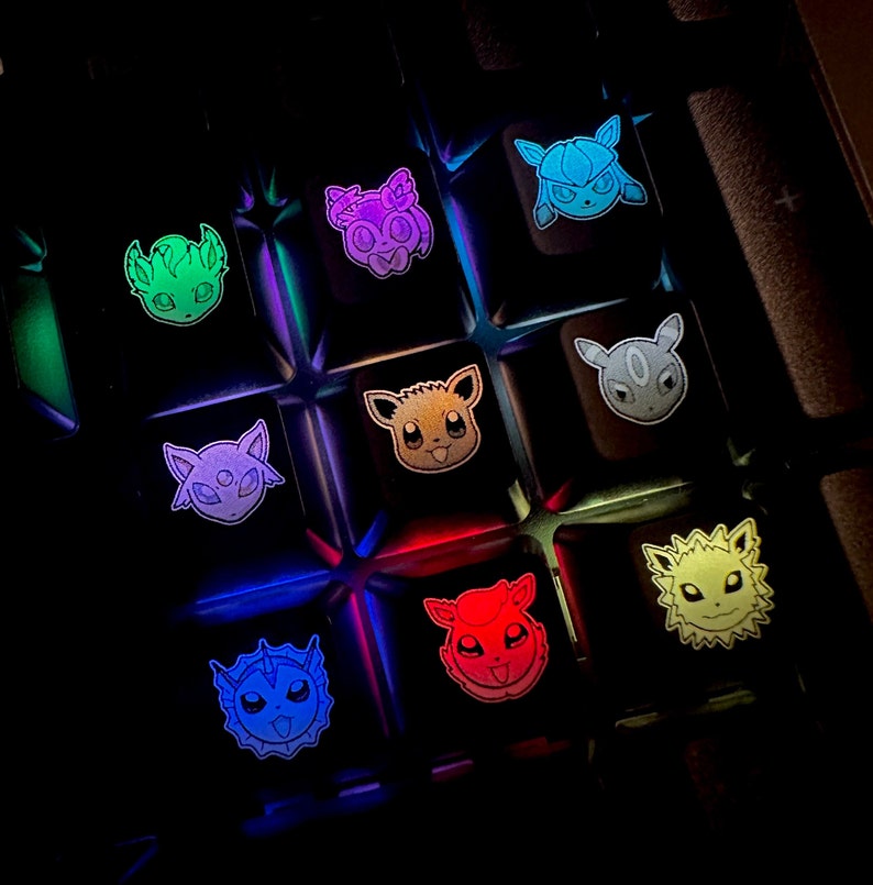 May include: A keyboard with custom keycaps featuring different Pokemon characters. The keycaps are illuminated with different colors, including green, purple, orange, red, blue, and yellow.