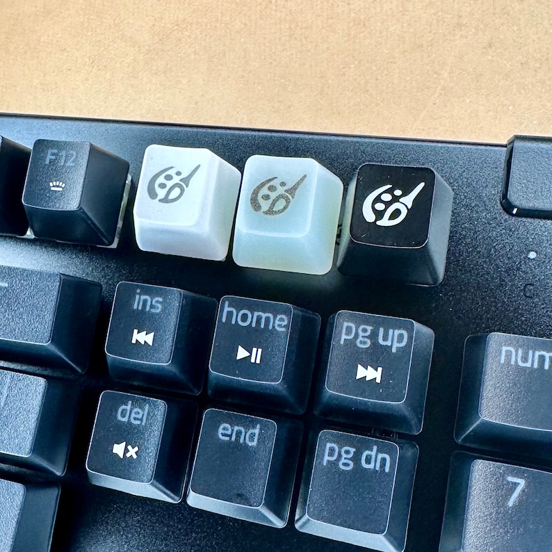 May include: A black keyboard with white keycaps featuring a paintbrush icon. The keycaps are labeled 'ins', 'home', 'pg up', 'del', 'end', and 'pg dn'.
