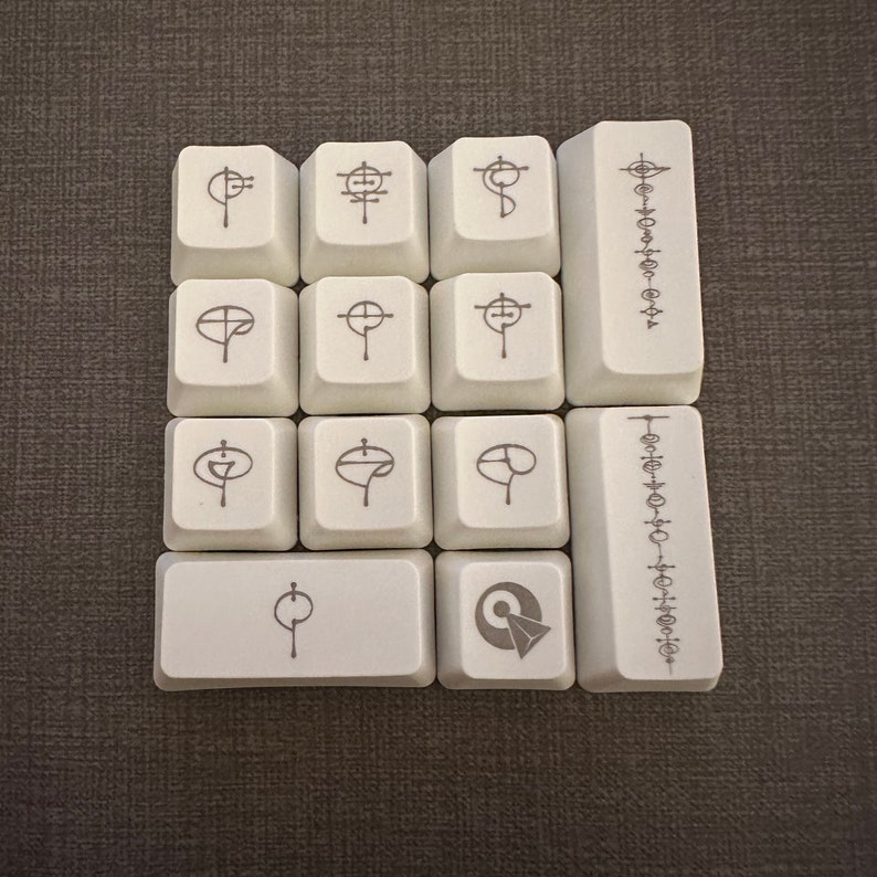 May include: A set of 10 white keycaps with various symbols and designs. The keycaps are arranged in a 3x3 grid with a single keycap below the grid. The keycaps are all white with black symbols and designs. The symbols and designs include a cross, a circle with a line through it, a circle with a dot in the centre, and a circle with a line through it and a dot in the centre.