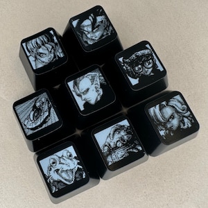 May include: Eight black keycaps with different pixelated images printed on them. The images include a frog, a person with a helmet, a person with a crown, a person with a sword, a person with a gun, a person with a hat, a person with a beard, and a person with a bow and arrow.