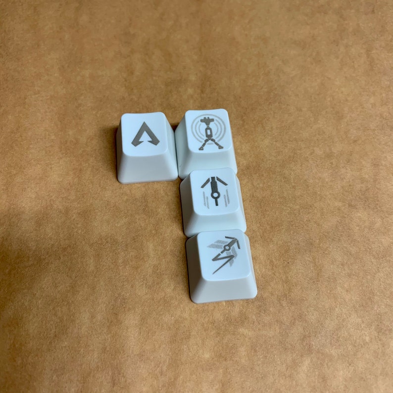 May include: Four white keycaps with different symbols printed on them. The symbols are a triangle, a circle with a cross inside, a person with arms outstretched, and a lightning bolt with an arrow.