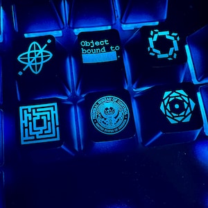 May include: A close-up of a blue mechanical keyboard with custom keycaps featuring various designs, including a maze, a seal of the Federal Bureau of Control, a geometric shape, and the text "Object bound to".