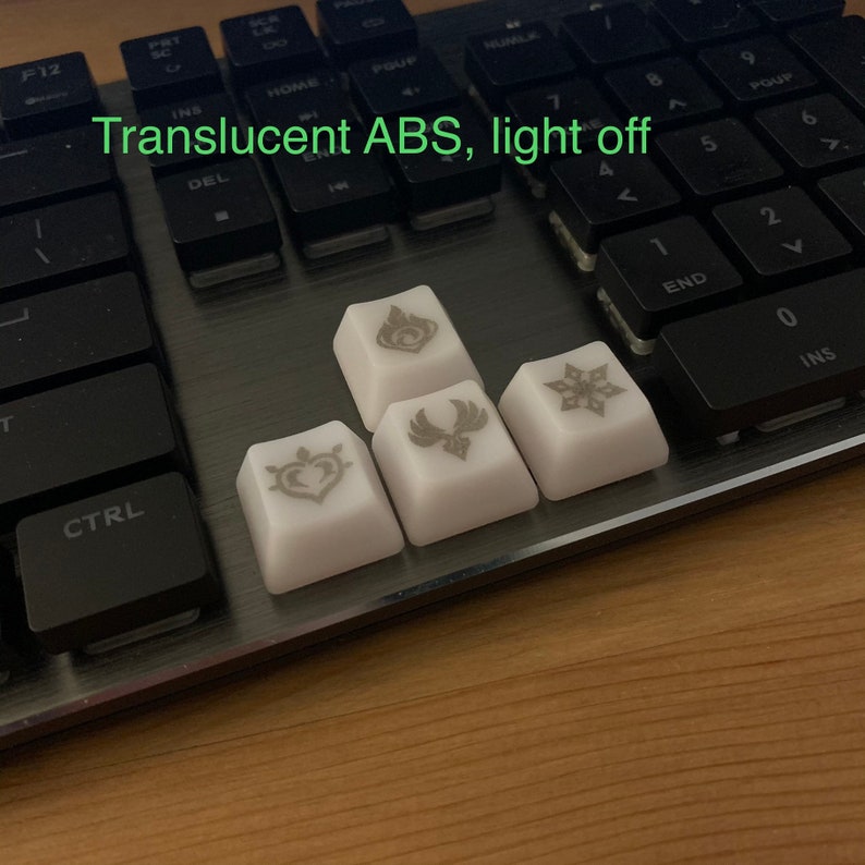 May include: Four white keycaps with different symbols printed on them. The keycaps are made of translucent ABS plastic and are shown with the lights off. The keycaps are sitting on a black keyboard.