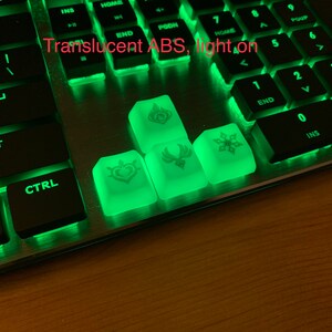 May include: Four translucent green keycaps with white symbols on a black keyboard. The keycaps are made of ABS plastic and have a light-up feature. The symbols on the keycaps are a heart, a phoenix, a snowflake, and a flame.