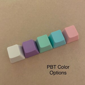 May include: Five different colored keycaps for a mechanical keyboard. The keycaps are in the colors white, purple, light green, light blue, and pink. PBT Color Options.