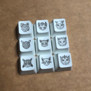 May include: Nine white keycaps with black and gray Pokemon character designs. The characters include Espeon, Umbreon, Flareon, Jolteon, Vaporeon, Leafeon, Glaceon, Sylveon, and  Eevee.