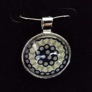 May include: A silver pendant necklace with a round glass charm featuring a blue and white geometric pattern.