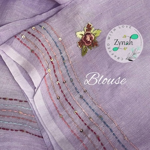 May include: A lavender blouse with a white trim and embroidered details. The trim features a row of gold sequins and colorful stitching. The embroidery includes a floral design and the text "Crafted with Love Zynah".