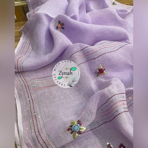 May include: A lavender linen scarf with embroidered flowers and sequins. The scarf has a border of sequins and a small logo that says "Crafted with Love Zynah".