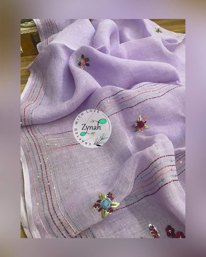 May include: A lavender linen scarf with embroidered flowers and sequins. The scarf has a border of sequins and a small logo that says "Crafted with Love Zynah".
