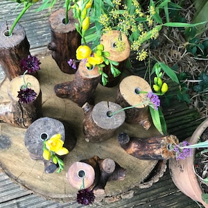 May include: A collection of rustic wooden log vases with holes drilled in the top, arranged on a wooden slice. The vases are filled with yellow and purple flowers.