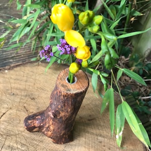 May include: A rustic wooden vase with a natural bark finish, featuring a single hole at the top for holding flowers. The vase is filled with yellow and purple flowers.