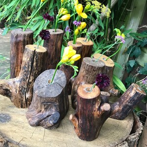 May include: A collection of rustic wooden vases, each with a unique shape and texture, are arranged on a wooden slab. The vases are filled with yellow and purple flowers.