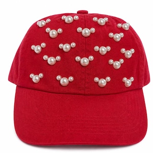 Op de afbeelding: Een felrode baseballcap versierd met talrijke witte imitatieparelclusters. De cap heeft een gebogen klep en een ronde kroon en biedt een stijlvol accessoire. De parels zijn in een herhalend patroon over het oppervlak van de cap gerangschikt.