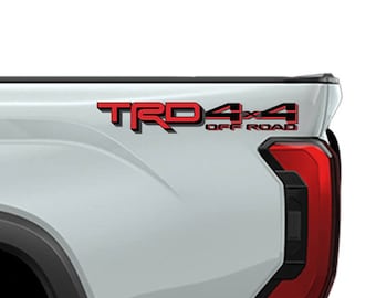 May include: A light gray truck bed with black trim and a black tire. The words "TRD 4x4 OFF ROAD" are in red. A sticker with a skull and the words "SUPDEC GRAPHIX" is on the side.