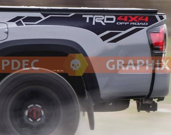 May include: A gray pickup truck with a black and gray "TRD 4X4 OFF ROAD" decal on the side. The truck has a black wheel with a red center cap.