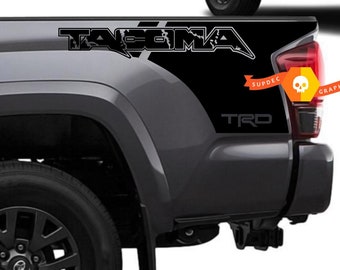 May include: Black and grey truck bed side decals with the word "TACOMA" in a stylised font and the word "TRD" in a smaller font. The decals are designed to be applied to the side of a truck bed.