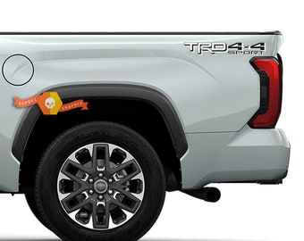 May include: A silver pickup truck with a black "TRD 4x4 Sport" decal on the side. The truck has a black wheel with a silver rim.
