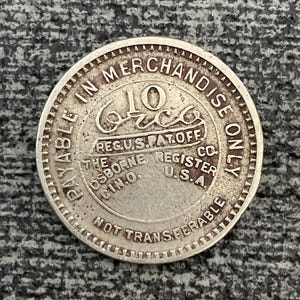 May include: A silver token with the text "PAYABLE IN MERCHANDISE ONLY" around the edge. The center of the token has the text "10¢" and "REG.U.S.PAT.OFF." and "THE OSBORNE REGISTER CO. CIN.O. U.S.A."  The token also has the text "NOT TRANSFERABLE" around the edge.