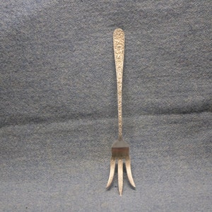 May include: A silver fork with a decorative, textured handle. The fork has three tines and is approximately 7 inches long.