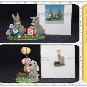 May include: Two gray bunny figurines, one holding a blue block with the letter 'G' and the other holding a red block with the letter 'S'. The bunnies are standing on a green base with flowers. The figurines are displayed on a white card with the text 'Pecks Antiques And Gift'.