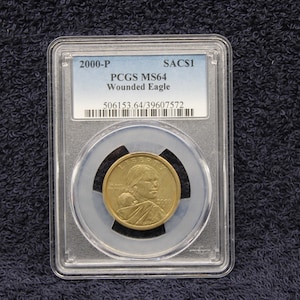 May include: A gold coin graded by PCGS as MS64, a 2000-P Sacagawea coin with the label "Wounded Eagle" and the grading number 506153.64/39607572.