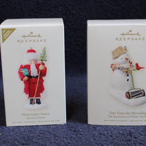 May include: Two Hallmark Keepsake Christmas ornament boxes. One features a Nutcracker Santa in a red coat, the other a snowman with a shovel. Text on the boxes reads "Nutcracker Santa" and "Sno Time for Shoveling".